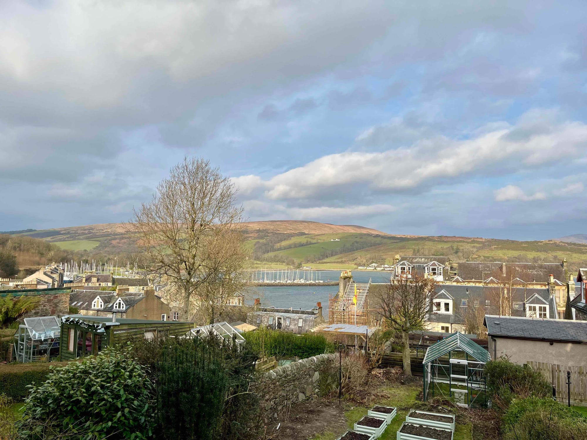 view of bay with sailboats at a marina, village houses, hills, and clouds in the sky