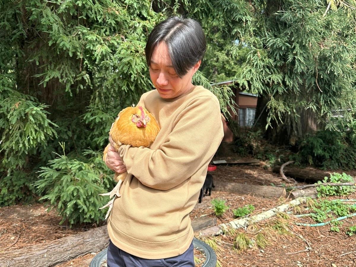 Avi holding a chicken in front of trees