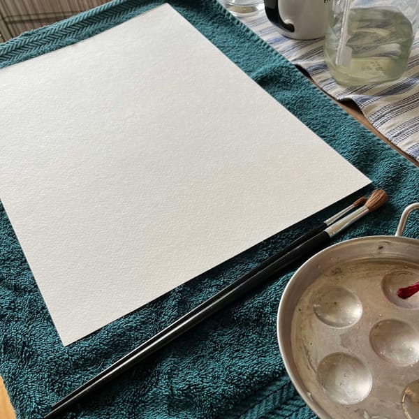A blank piece of paper, paintbrushes, and a round metal palette