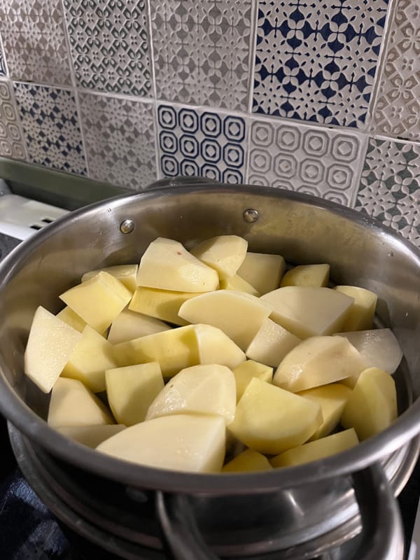 Pieces of potato in a metal steamer against a tiled backdrop. 