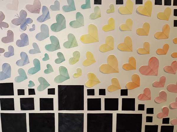Watercolour hearts, a butterfly, and black squares arranged on a wall. 