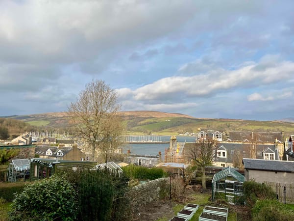 view of bay with sailboats at a marina, village houses, hills, and clouds in the sky