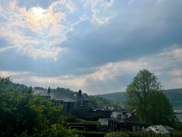 The sun streaming through the clouds over trees and houses, the rays visible in the mist.